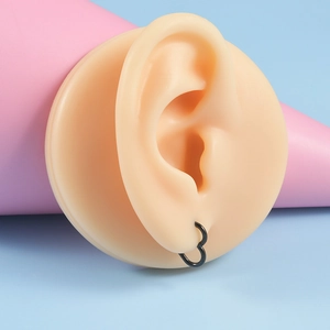 Gros plan d'une boucle d'oreille cœur en acier inoxydable noir portée sur un modèle d'oreille