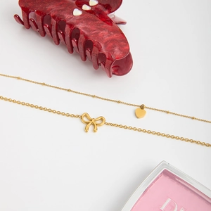 Detailed macro view of gold layered bow and heart pendant necklaces with beaded chain
