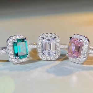Macro view of three halo rings with emerald-cut gems in green, white, and pink