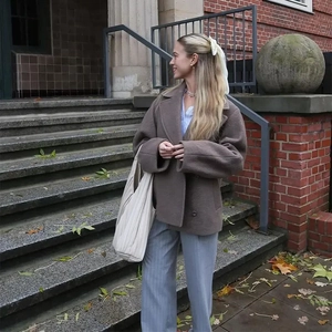 Detail view of brown double-breasted wool coat styled with white tote bag and blue trousers