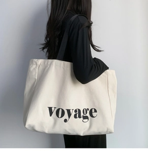 Close-up of large canvas tote bag with black voyage text on a minimalist cream fabric