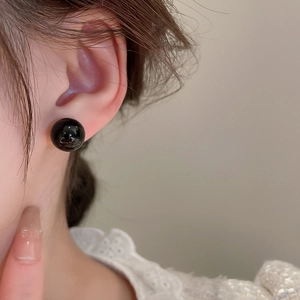 Close-up of a model wearing a minimalist black bead stud earring with a glossy finish