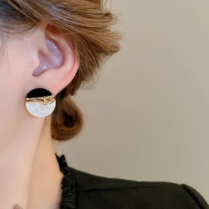 Détail d'une boucle d'oreille ronde en résine avec bordure dorée, émail noir et nacre