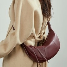 Detail view of burgundy leather crescent bag with tassel zipper on a beige coat