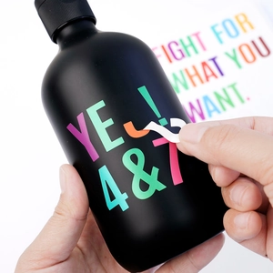 Applying colorful self-adhesive vinyl letter stickers on a black matte bottle surface