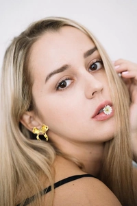 Close-up of golden bow stud earrings on model's ear with high polish metal finish
