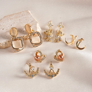 Ten-piece gold earring set with moon, teddy bear, and square zircon studs on silk