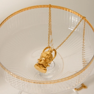 Golden Sun Wukong pendant necklace in 18K stainless steel on a vintage glass cup