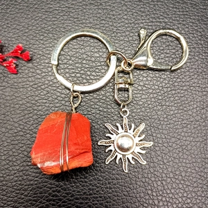 Detail of red crystal stone wrapped in wire with silver sun pendant on a keychain