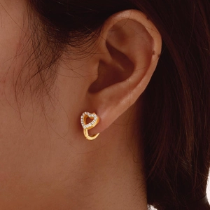 Detail of heart-shaped gold earring with pavé-set crystals on model's ear lobe