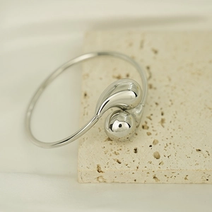 Macro shot of silver teardrop bangle on travertine stone with high-polish mirror finish