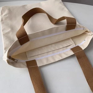 Detail of canvas tote bag showing zipper closure and internal mobile phone pocket