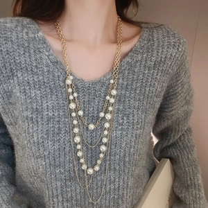 Detail of layered gold chain necklace with white faux pearls over a gray sweater