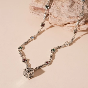 Close-up of vintage square pendant with floral relief and colorful gemstone chain links