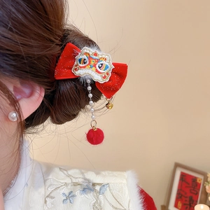 Detail of red velvet bow hair clip with embroidered lion dance motif and plush ball