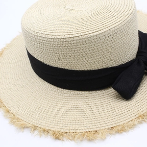 Detail of raffia boater hat with black ribbon bow and frayed edge fringe texture