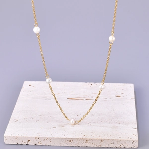 Minimalist gold chain necklace with five white freshwater pearls on a stone base