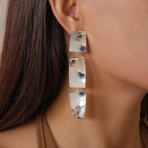 Macro shot of silver three-tier rectangular geometric earrings worn by a model