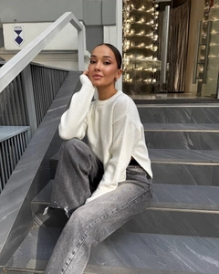 Detail of white crew neck sweater with side slit hem and ribbed cuffs on model