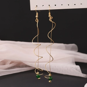 Detail of gold spiral wave earrings with green bead accent on elegant fabric