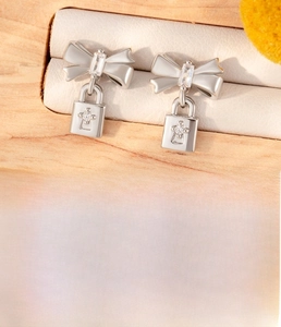 Detail of silver bow lock earrings in titanium steel with zircon on a wood jewelry box