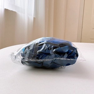 Detailed view of a navy blue satin scrunchie packaged in a clear protective plastic bag