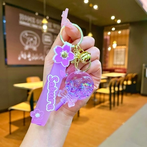 Handheld detail of purple Sakura liquid shaker keychain with glitter and golden bell