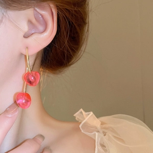Close-up of red cherry dangle earrings worn by model with gold metal accents
