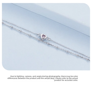 Macro detail of a double-layered S925 silver bracelet featuring a pink heart pendant