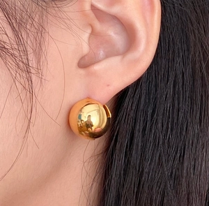 Close-up of polished golden spherical earrings worn on the ear showing size and texture