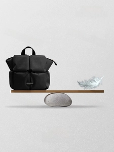 Détail d'un sac à dos matelassé noir léger sur une planche en bois avec une plume blanche