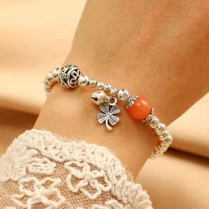 Detailed close-up of retro silver beaded bracelet with clover charm and bell pendant