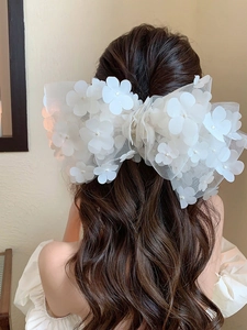 Detail of a large white tulle bow hair clip with floral 3D accents on long wavy hair