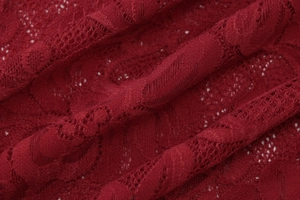 Detailed close-up of dark red lace fabric with intricate floral patterns and textures