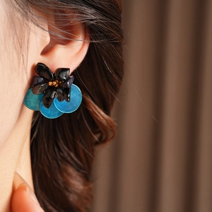 Close-up of vintage floral earrings with black petals and blue dangles on a model's ear