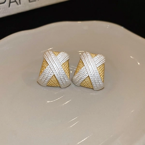 Detail of gold and silver square woven earrings on a white ceramic plate