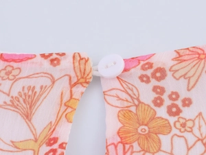 Dettaglio di un bottone bianco e del tessuto in chiffon floreale di un abito rosa