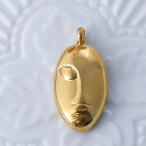 Detailed close-up of a 24k gold plated abstract face mask pendant on a white plate