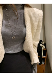 Close-up of a silver geometric drop pendant necklace styled with a white tweed jacket