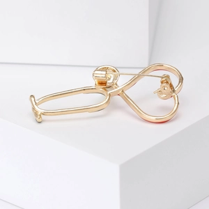 Golden stethoscope heart brooch with red enamel on a clean white geometric background