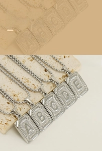 Detail of square stainless steel letter pendants with radial textures on pearl chains