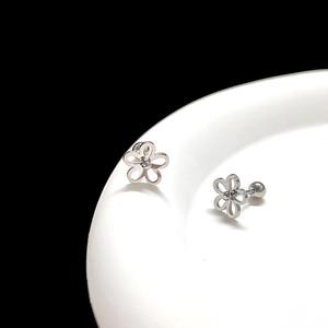 Macro shot of silver hollow flower stud earrings with screw backs on white ceramic