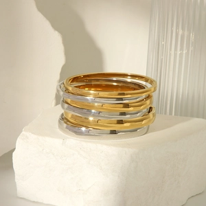Polished 18K gold and silver titanium steel bangles stacked on white stone surface