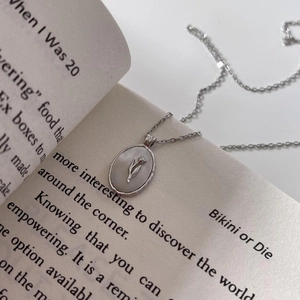 Close-up of silver oval pendant with embossed tulip and mother of pearl on book