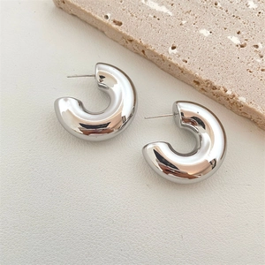 Detailed view of chunky silver C-shaped hoop earrings on a textured stone background
