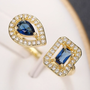 Detail of gold open ring with teardrop and square dark blue stones with halo setting
