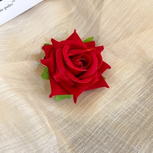 Close-up of a large red velvet fabric rose hair clip with green leaves on gold satin