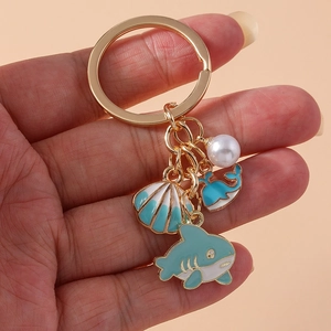 Gold ocean keychain featuring blue enamel whale, shell, shark charms and a faux pearl