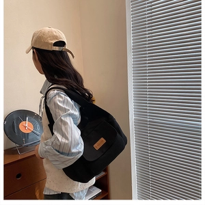 Side view of a black canvas tote bag worn by a model in a cozy indoor lifestyle setting