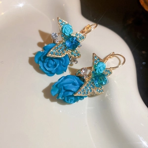 Close-up of vintage blue rose earrings with crystal-encrusted butterfly and gold finish